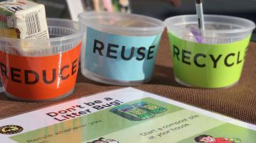 Eco Challenge Photo. Picture of  and elementary school desk, showing three cups with the words: reduce, reuse and recycle.