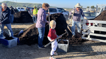 Little boy with family helping shovel compost into bucket.