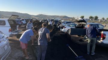 Orange County residents scooping compost with shovesl into cars in front of large pile of compost.