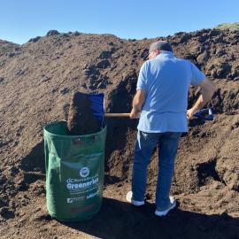 Man shoveling compost into green bin.