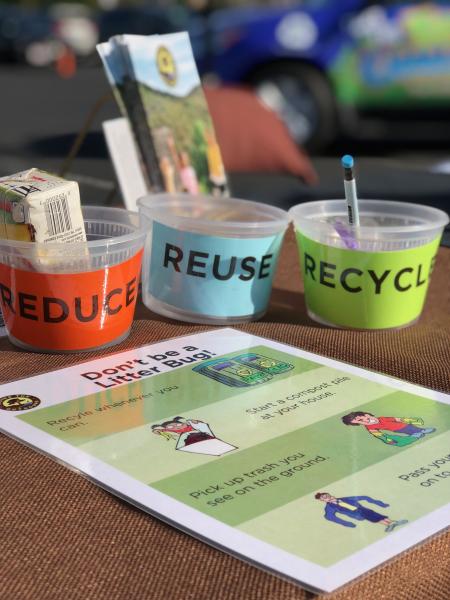Eco Challenge Photo. Picture of  and elementary school desk, showing three cups with the words: reduce, reuse and recycle.
