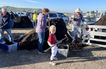Little boy with family helping shovel compost into bucket.