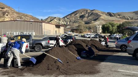 OC Residents using shovels to pick up compost on a tall pile at a landfill site