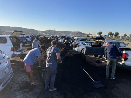 Orange County residents scooping compost with shovesl into cars in front of large pile of compost.