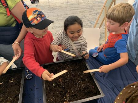 Three young children looking at worm composting. 